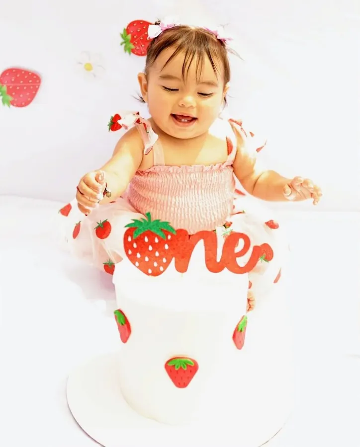 First birthday cake smash, laughing behind a strawberry cake