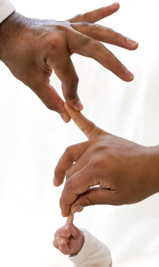 Parents' hands linked finger to finger down to their newborn's tiny grip