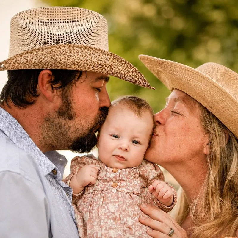 Family session, parents in cowboy hats kissing their baby